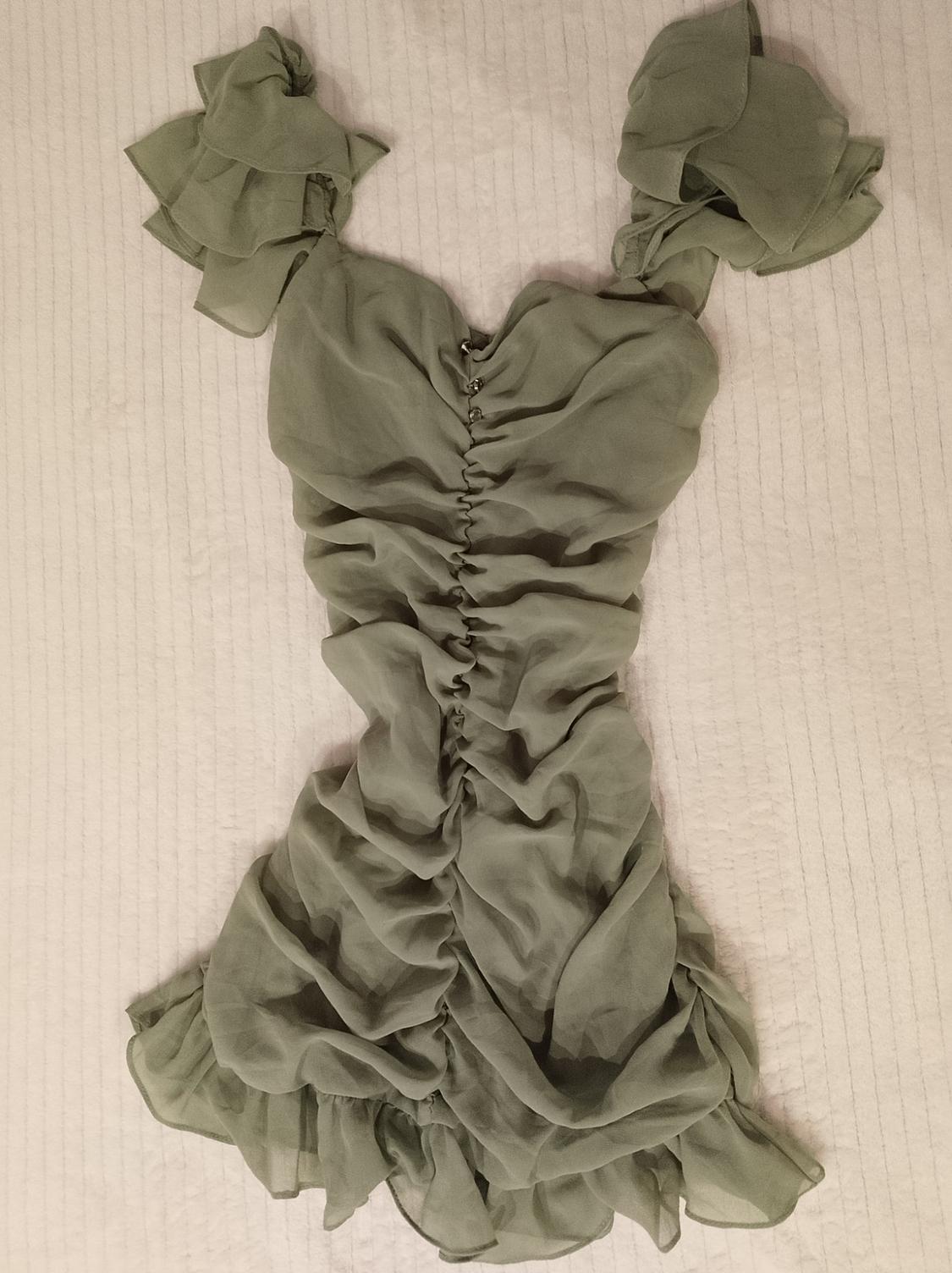 Light green short dress with ruffles, sweetheart neckline, and central button-up ruched detailing, laid out on a textured white surface.