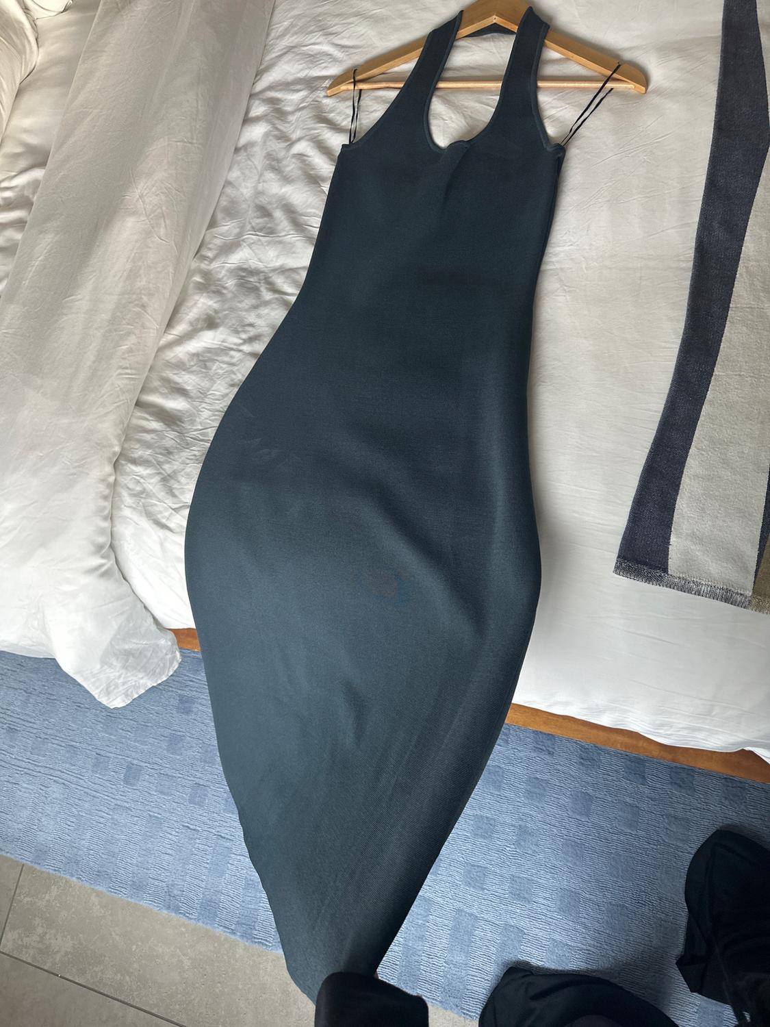 Sleeveless black dress on a white bed, hanging on a wooden hanger. Blue rug and towel to the right.