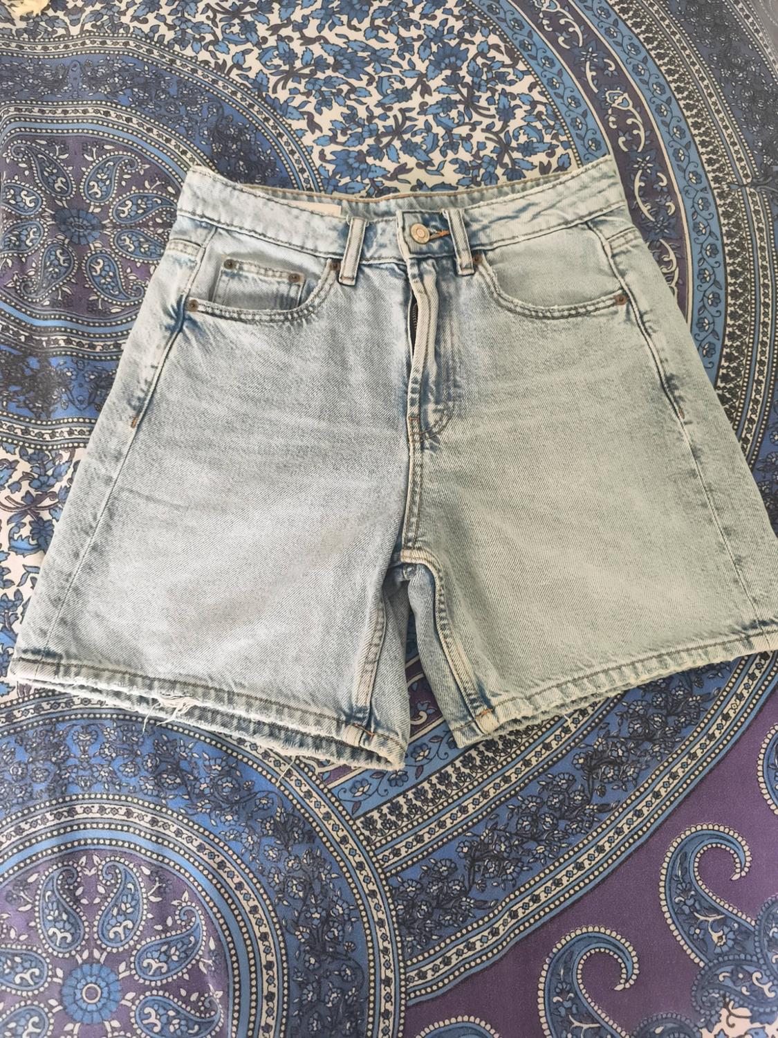 Light-blue denim shorts with a frayed hem, over fabric with a print in blue and purple tones.