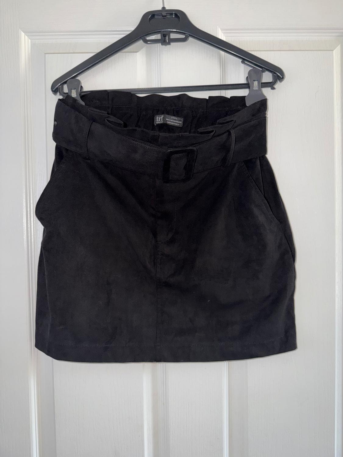 Black skirt hanging on a hanger over a white door. It has a wide waistband and a simple, elegant design.
