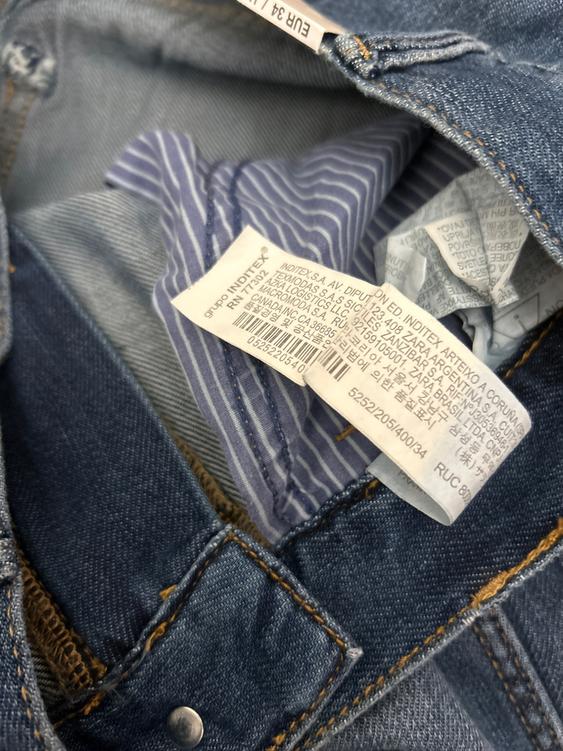 Blue jeans label with visible stitching and blue and white striped lining. Text on label: "INDITEX S.A. AV. DIPUTACIÓN".