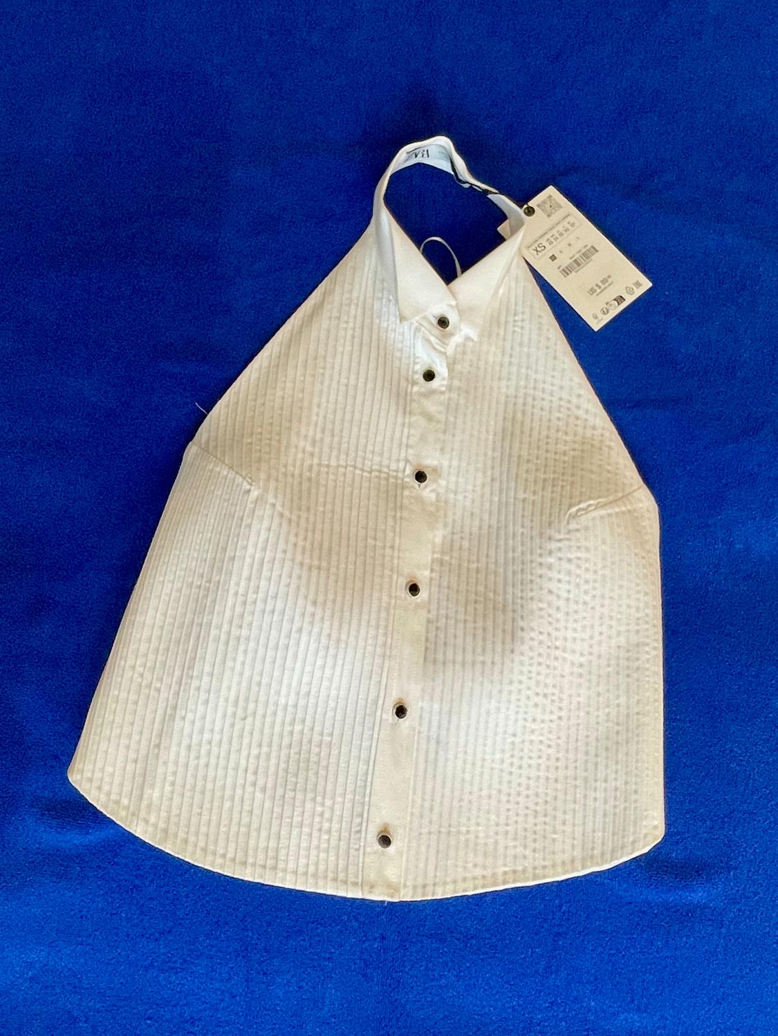White sleeveless shirt with black buttons on a blue background. Visible tag with XS size details and price.