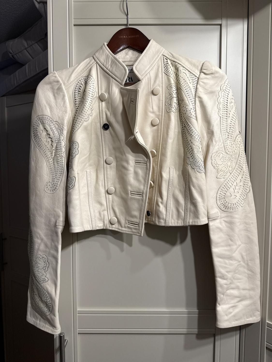 White short jacket with embroidery on the sleeves, hanging on a wooden hanger with the "Laura Ashley" brand in a closet.