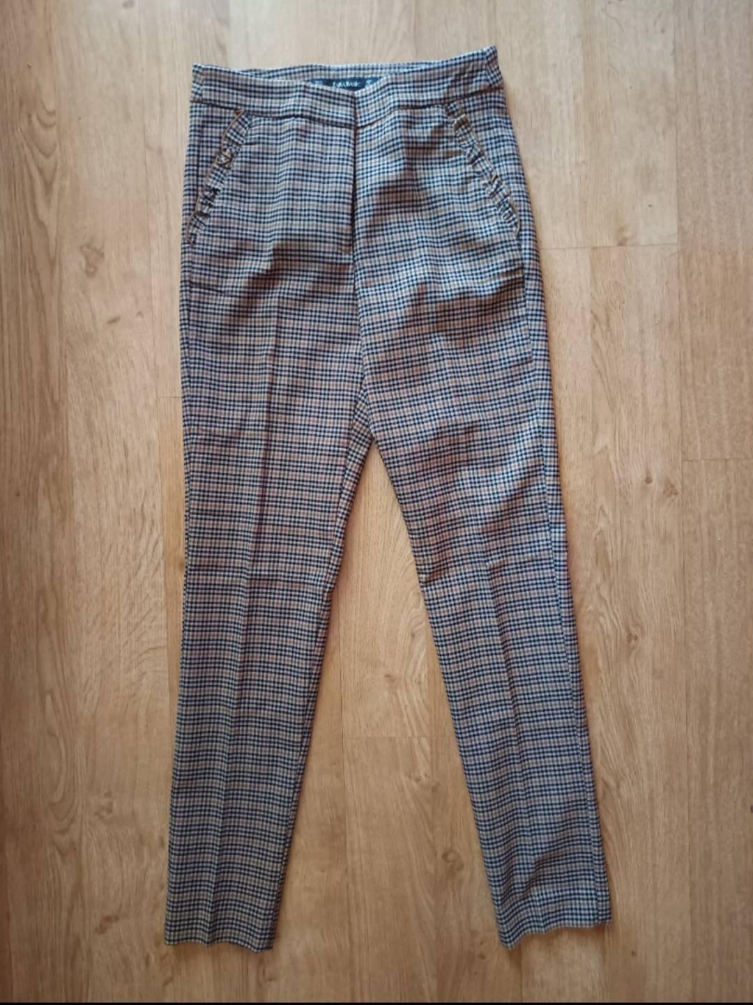 Straight-leg trousers with a checked pattern in brown and black tones, laid out on a light wooden floor.