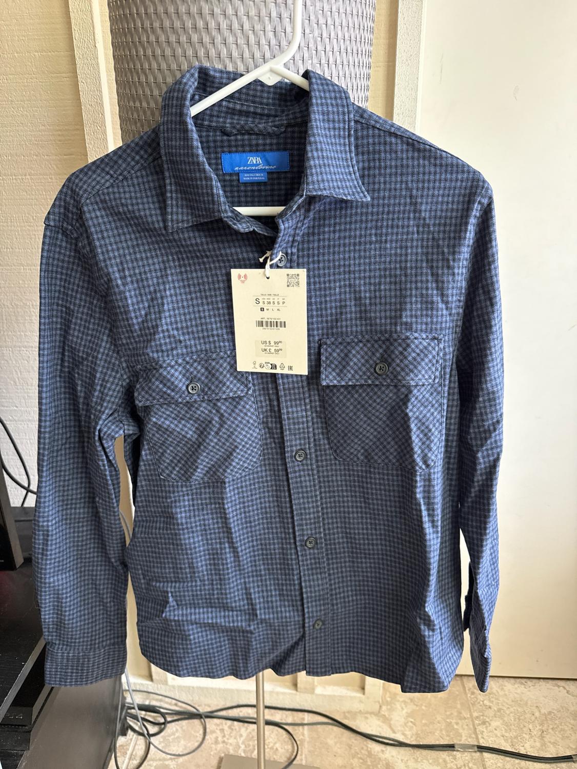Blue checked shirt with pockets, hanging on a hanger. Visible text: ZARA, S, US $99.90, UK £59.99.