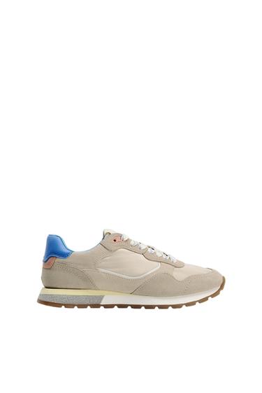 Beige trainers with blue and pink detailing, brown sole, and white laces, on a white background.