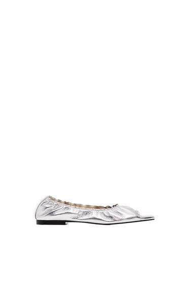 Side view of a silver flat shoe with ruched texture and a black sole.