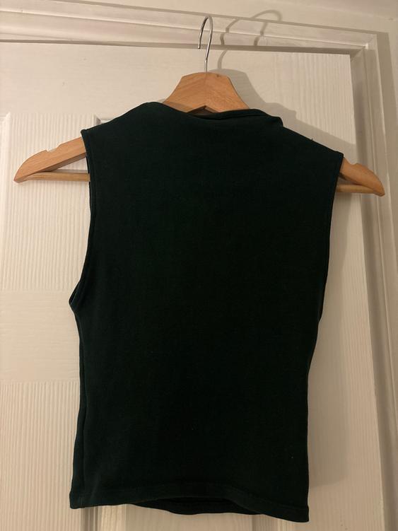 Black sleeveless waistcoat hanging on a wooden hanger over a white door.