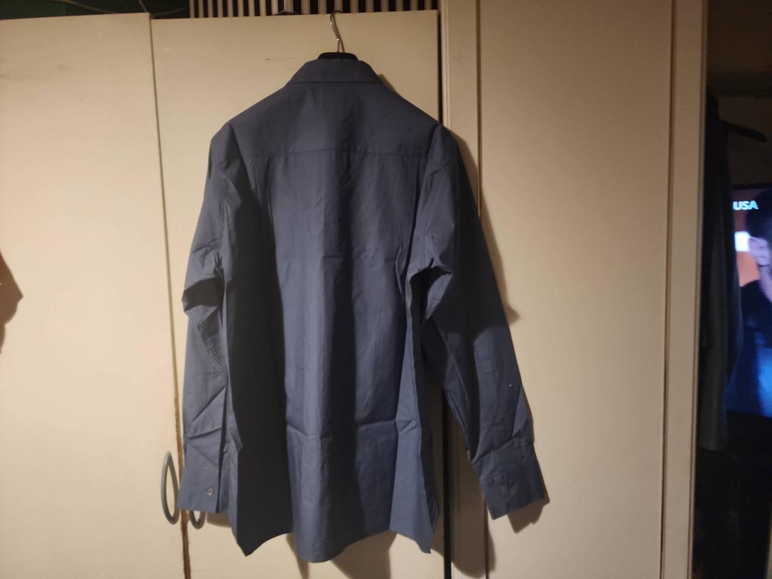 Rear view of a long-sleeved blue shirt hanging in front of a wardrobe. Relaxed atmosphere. In the background, a screen with the text USA.