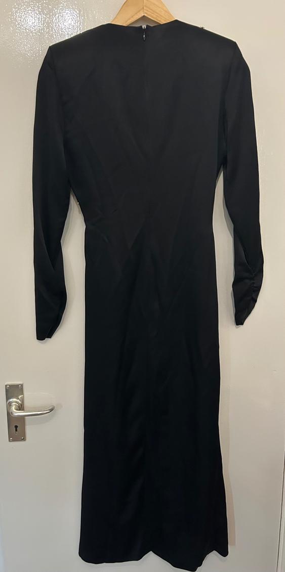 Black long-sleeved dress hanging on a wooden hanger over a white door. Rear view of the simple and elegant design.
