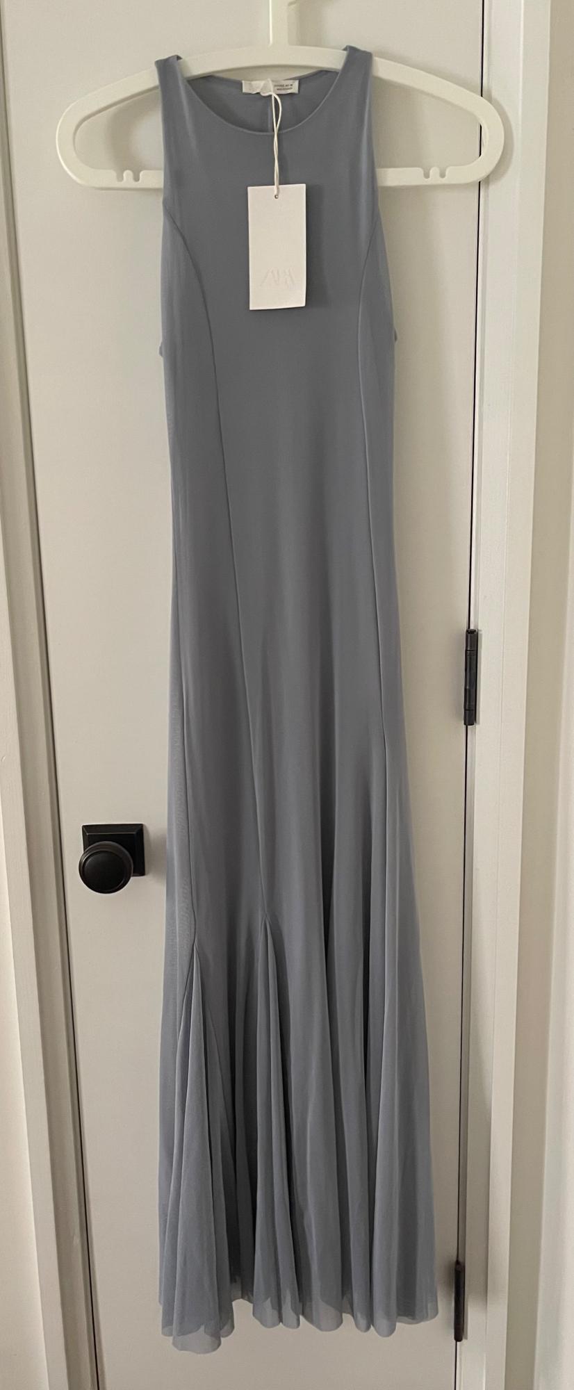 Greyish-blue sleeveless maxi dress hanging on a hanger over a white door with a black knob. Visible label with the text ZARA.
