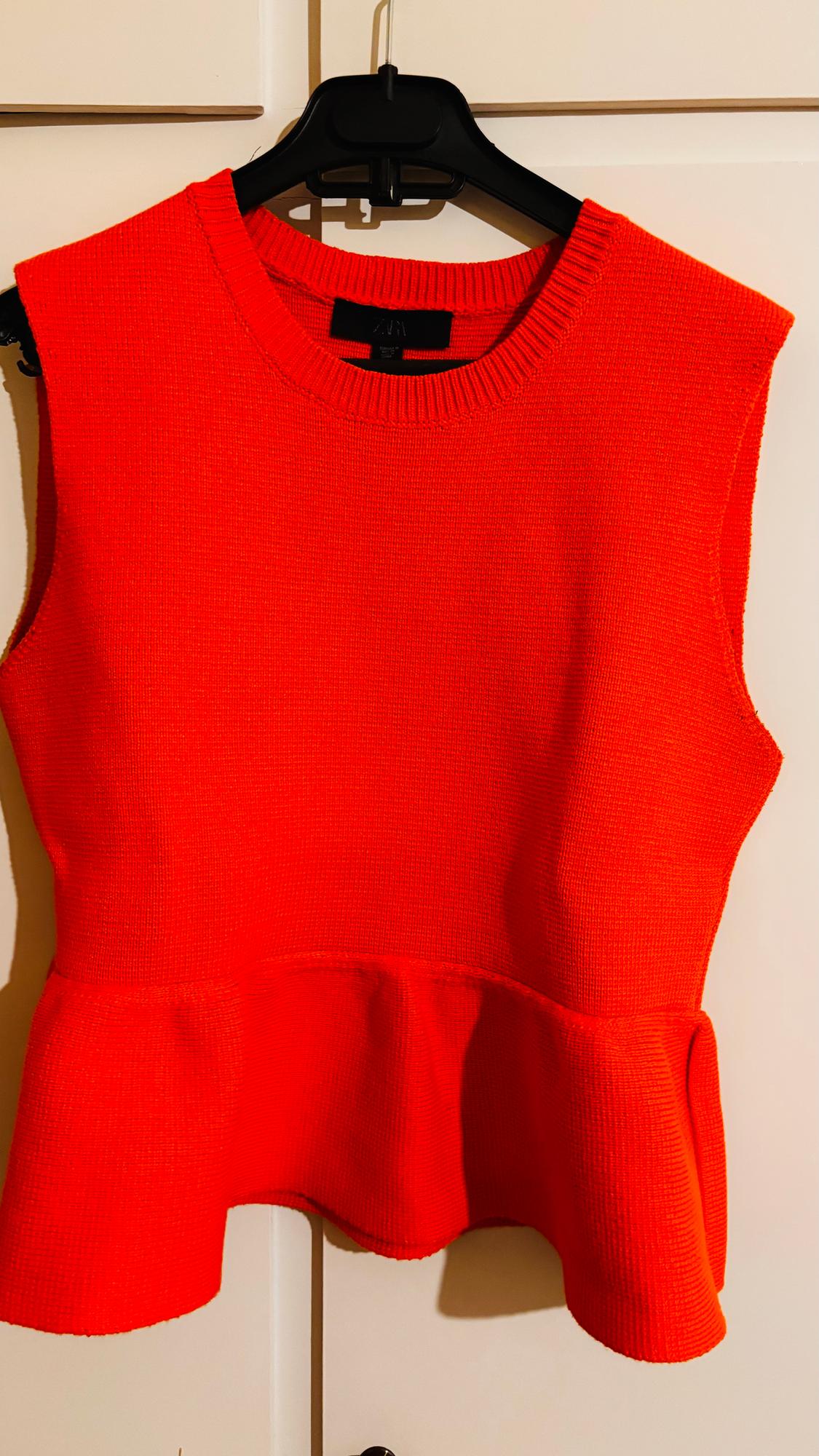 Red sleeveless top with a round neck and frill detail at the waist, hanging on a black hanger against a light background.