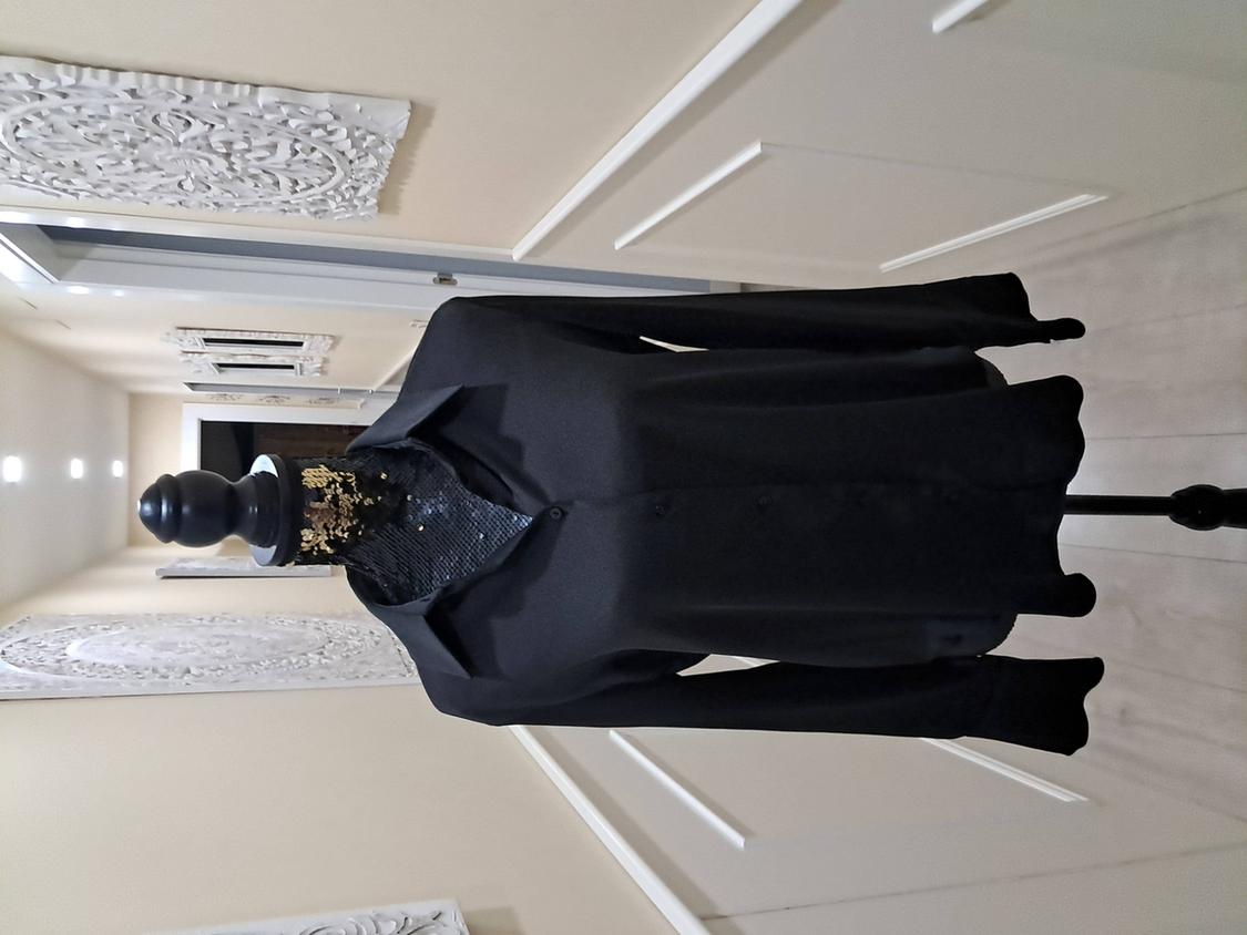 Mannequin in a black button-down collared shirt, in a lit corridor with white decorations on the walls.