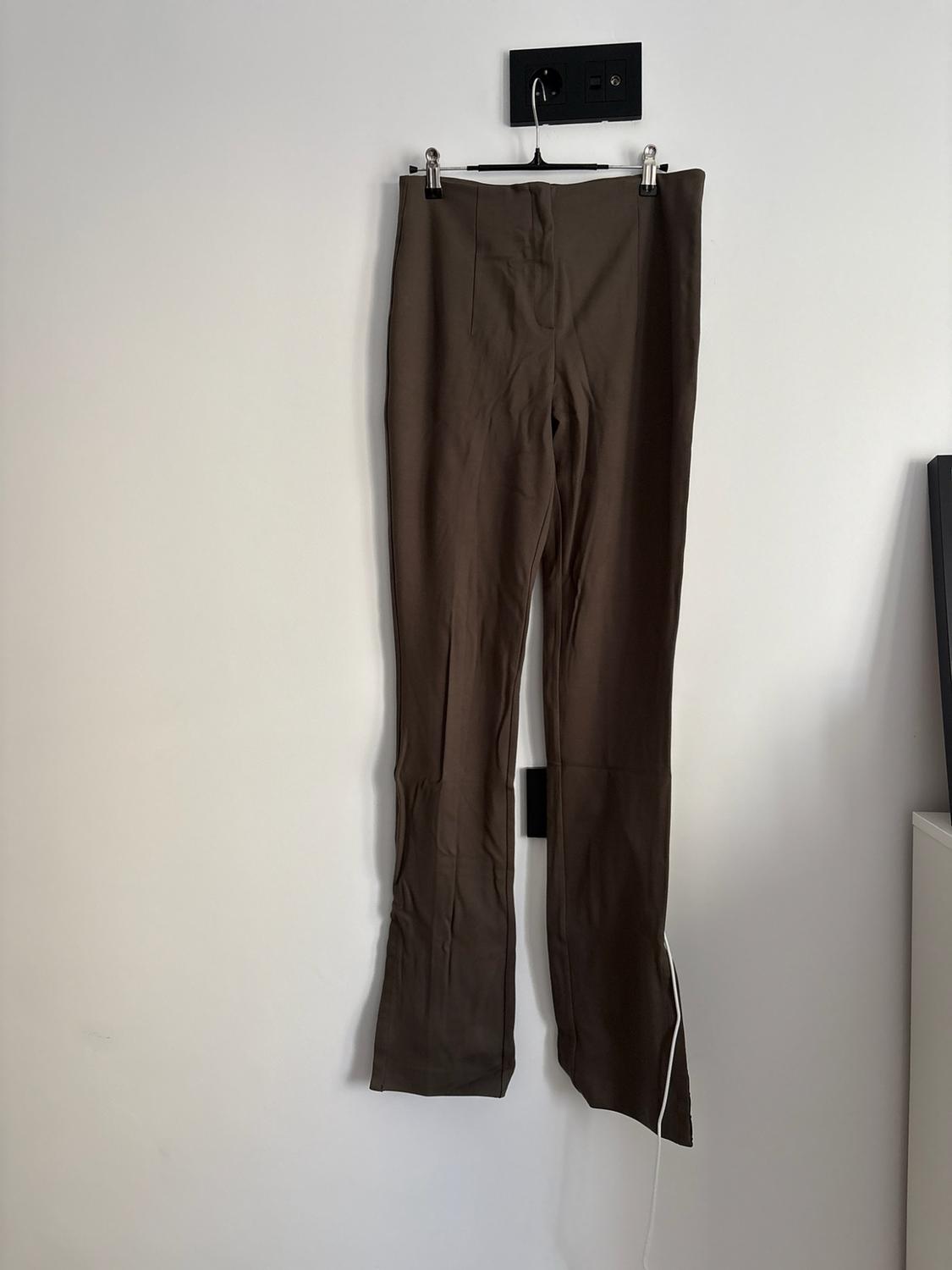 Brown trousers hanging on a hanger against a white wall. Casual and relaxed style in an everyday setting.