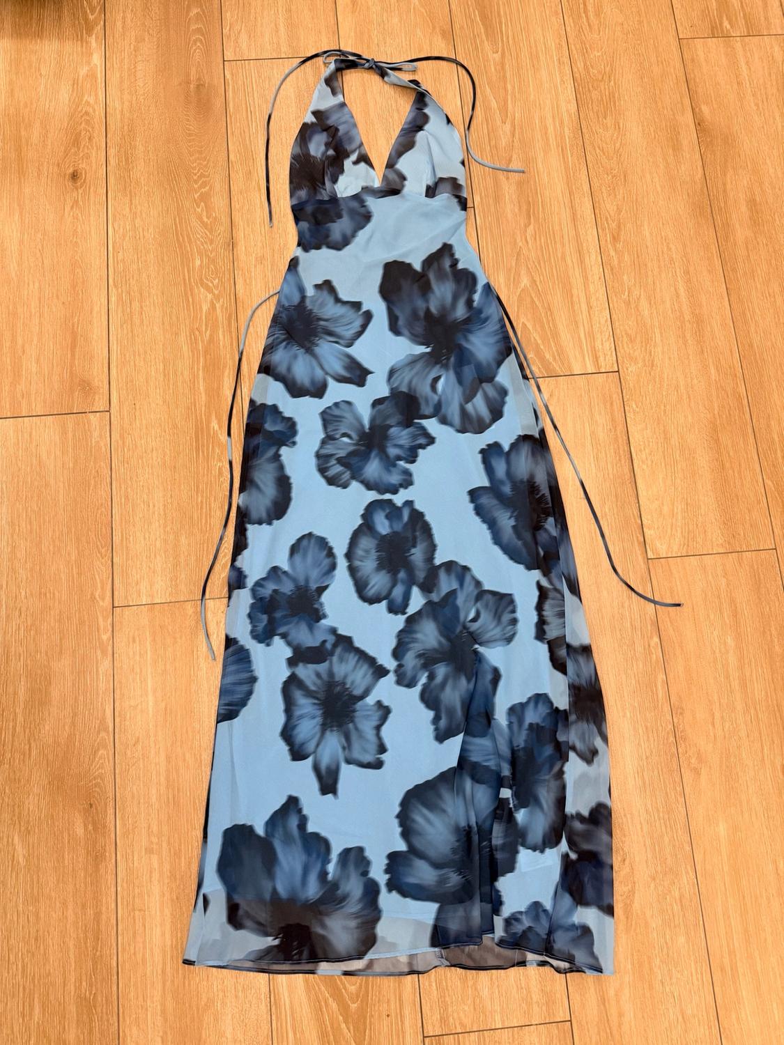 Long light-blue dress with large dark flowers, a halter neckline and thin straps, laid out on a wooden floor.