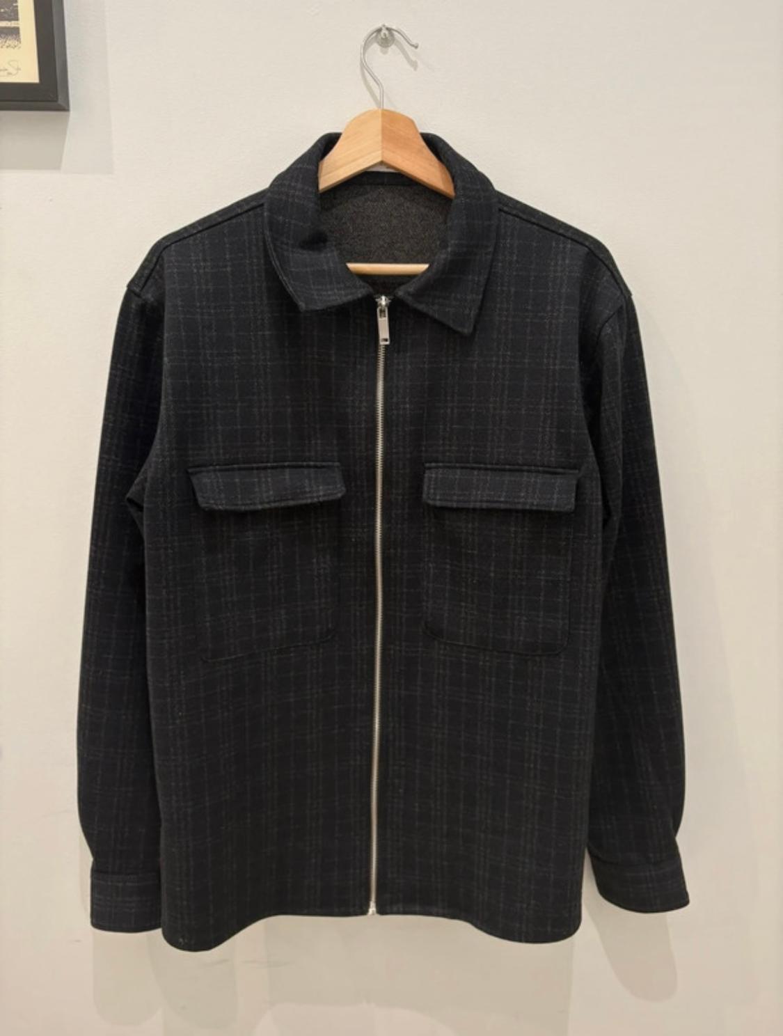 Black zip-up jacket with front pockets, hanging on a wooden hanger against a white background.