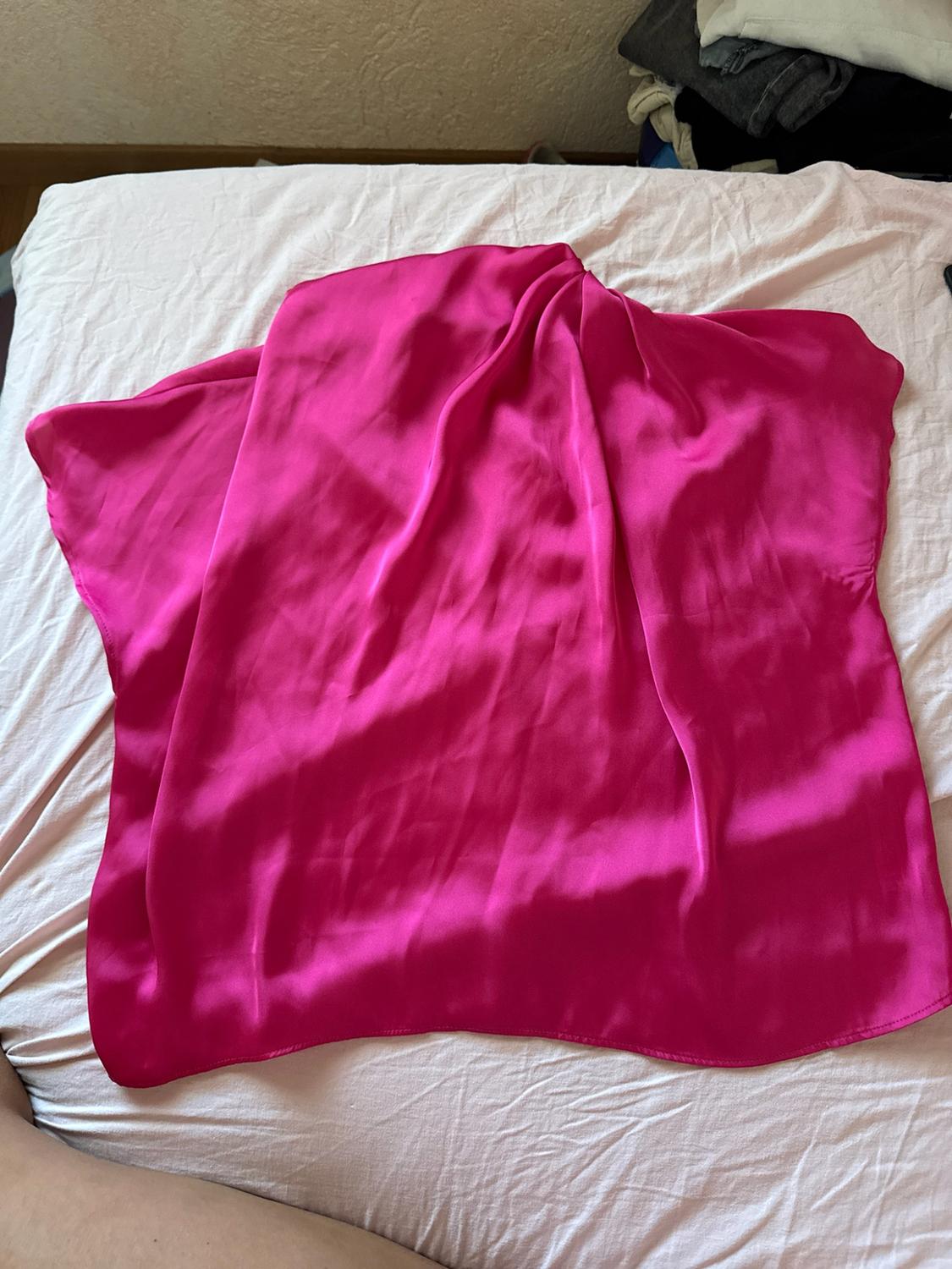 Bright fuchsia satin garment laid out on a bed with light-coloured sheets. Casual setting with folded clothes in the background.
