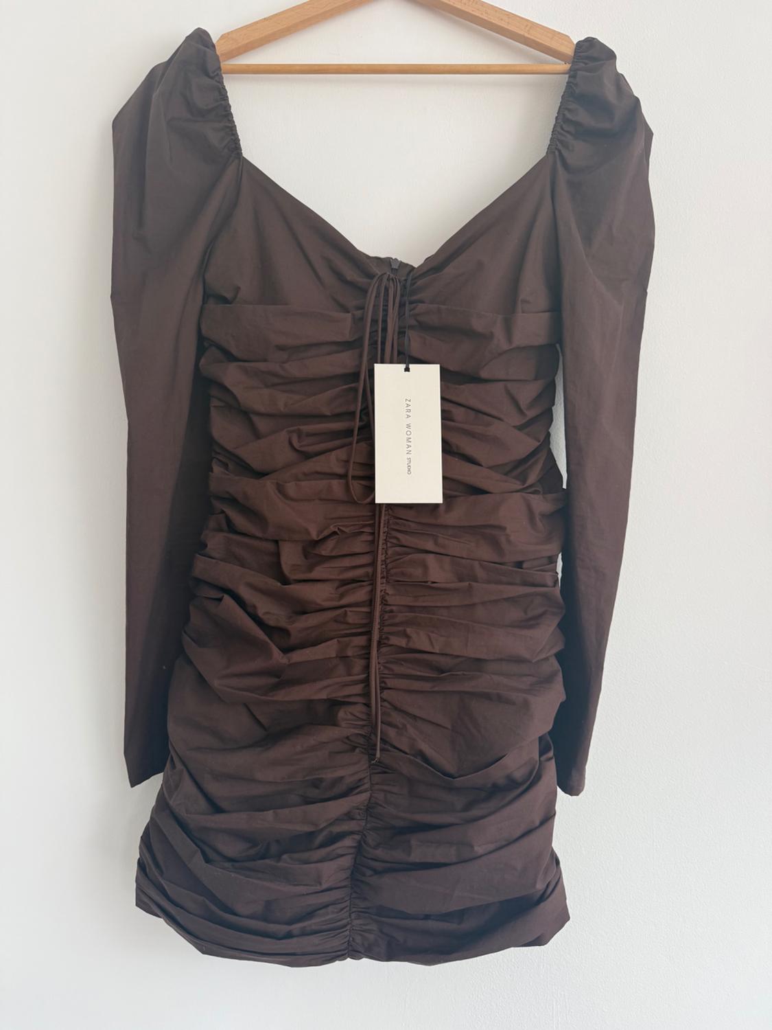 Brown ruched dress with long sleeves hanging on a wooden hanger. Label visible with text: "ZARA WOMAN".