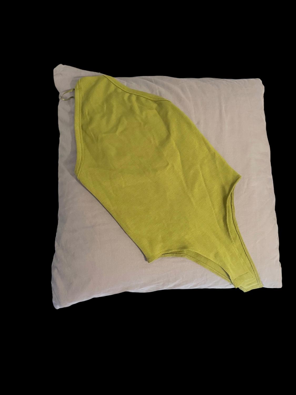 Pistachio-green sleeveless bodysuit laid out on a light beige pillow, against a black background.