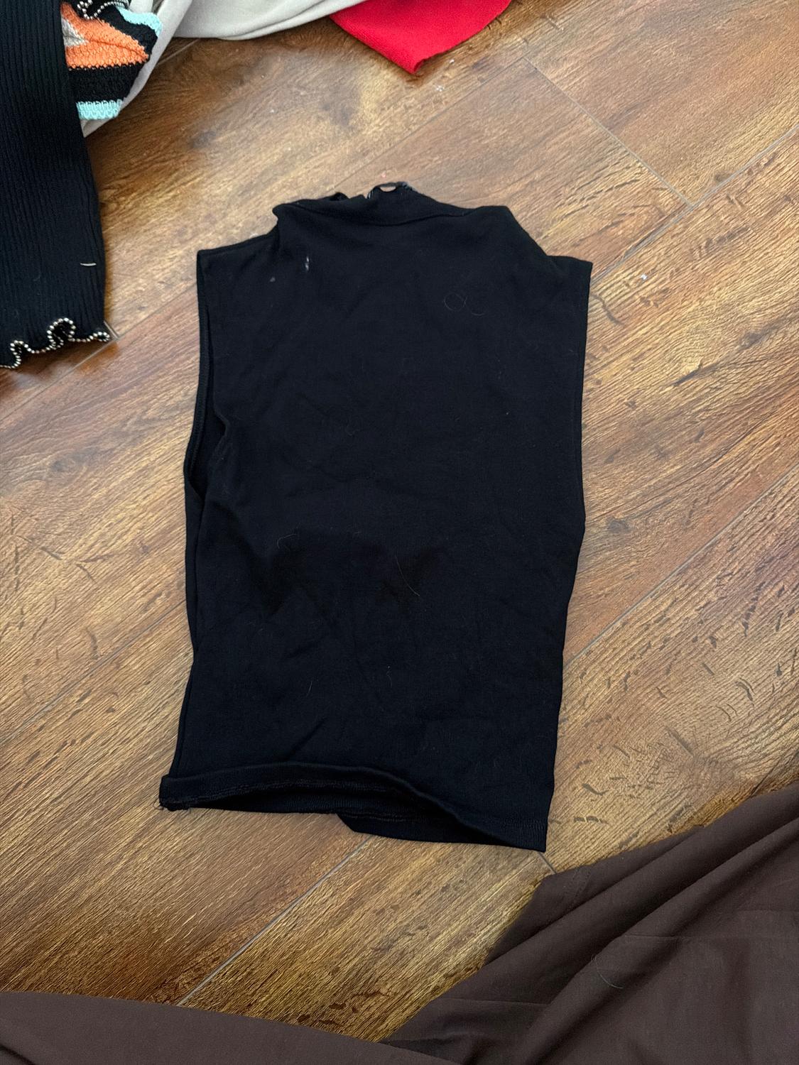 Black vest top folded on a wooden floor, surrounded by red, beige, and black garments with detailing.