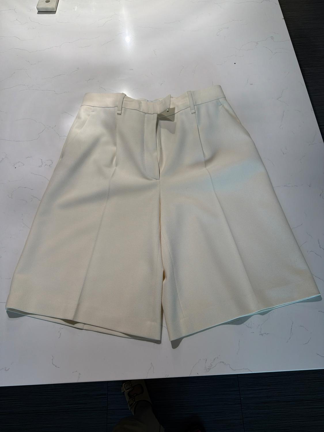 Wide-leg tailored Bermuda shorts with pleats, laid out on a white marble surface in a relaxed style.