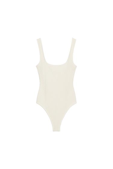 Front view of a white fitted bodysuit with a square neckline and wide straps. Structured design and snap closure at the bottom.