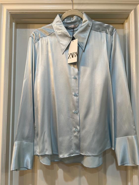 Light blue satin shirt hanging on a hanger with a Zara tag. White door background.