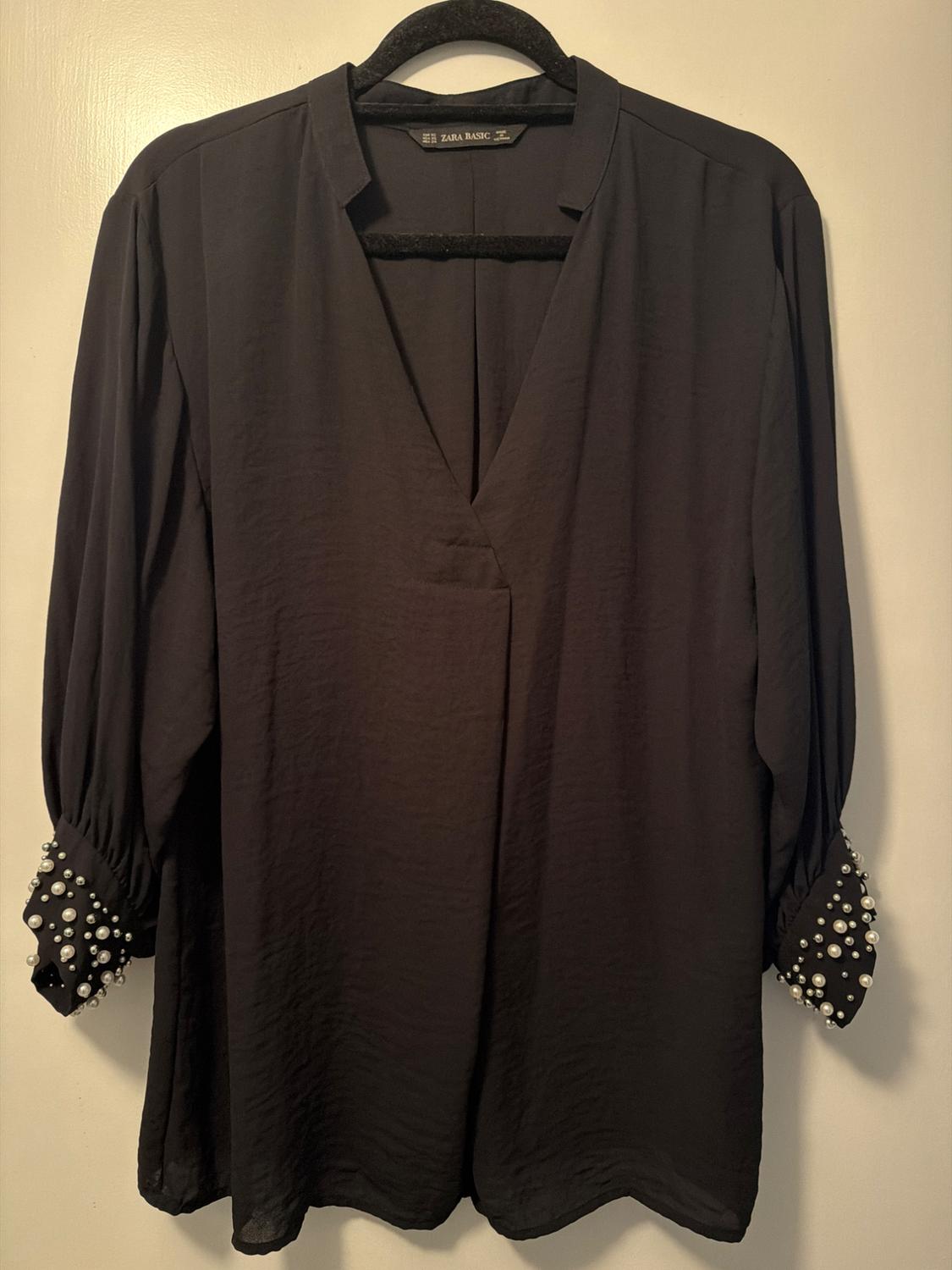 Black long-sleeved blouse with white pearl-embellished cuffs, hanging on a black hanger. Label: ZARA BASIC.