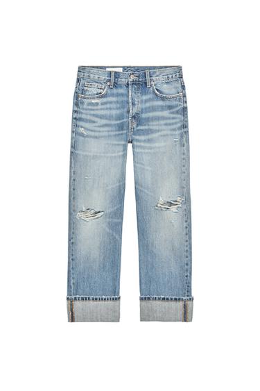 Front view of straight blue jeans with rips, five pockets, and turn-up hems. Front fastening with metal buttons.