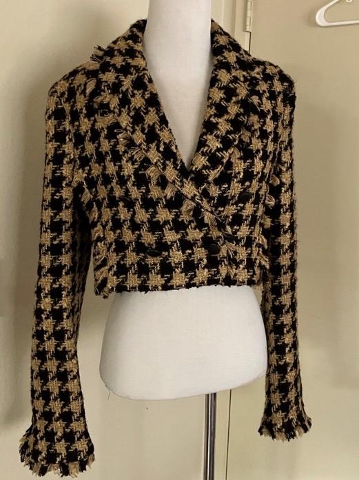 Black and beige checked short jacket on a white mannequin, with wide lapels and long sleeves, in an indoor setting.