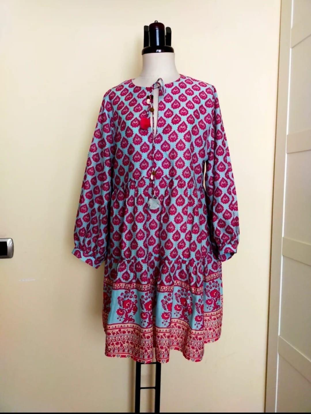 Printed dress in red and blue tones with tassel details, displayed on a mannequin against a beige background.