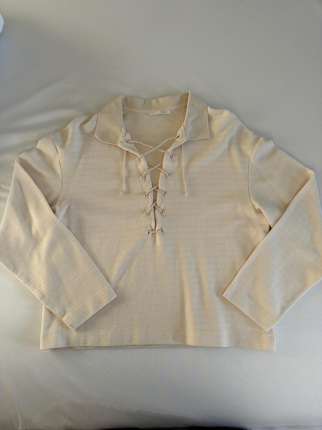 Beige long-sleeve shirt with a collar and lace-up front, photographed flat on a white fabric surface.