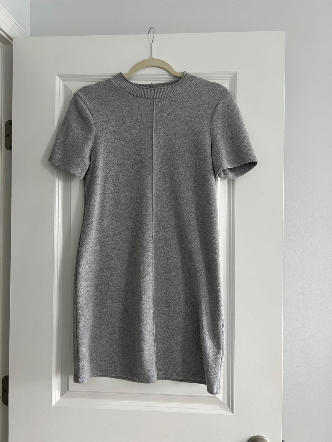 Short-sleeved gray dress hanging on a hanger over a white door. The design is simple and minimalist.