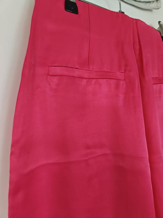 Fuchsia trousers hanging on a hanger, showing details of back pockets and soft texture. White background.