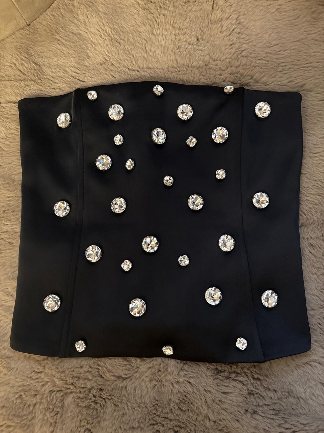 Black top with sparkling rhinestones on a beige fluffy fabric background. Elegant and eye-catching design.