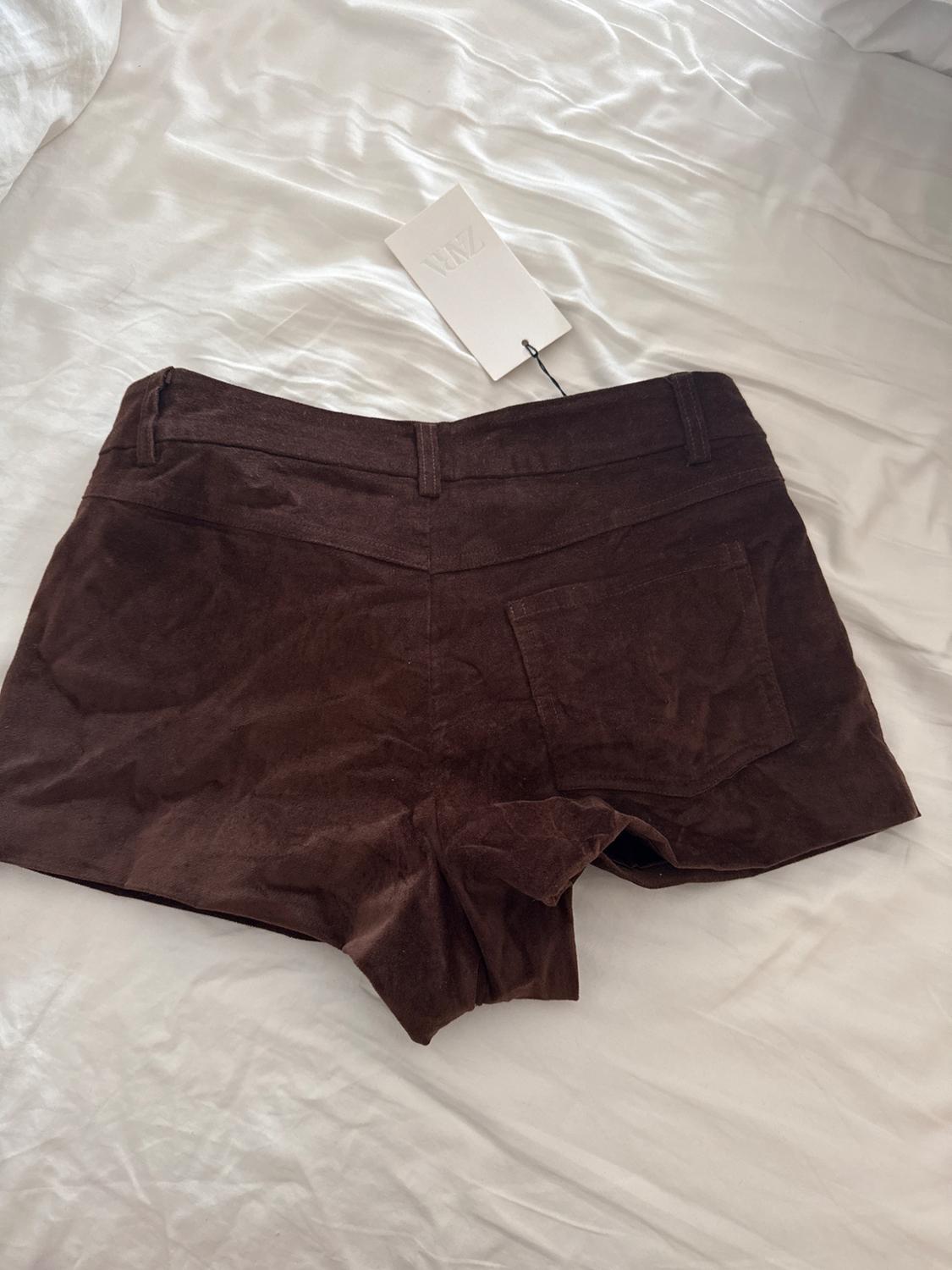 Soft brown fabric shorts on a white bed, with a hanging tag that says "YAZ".