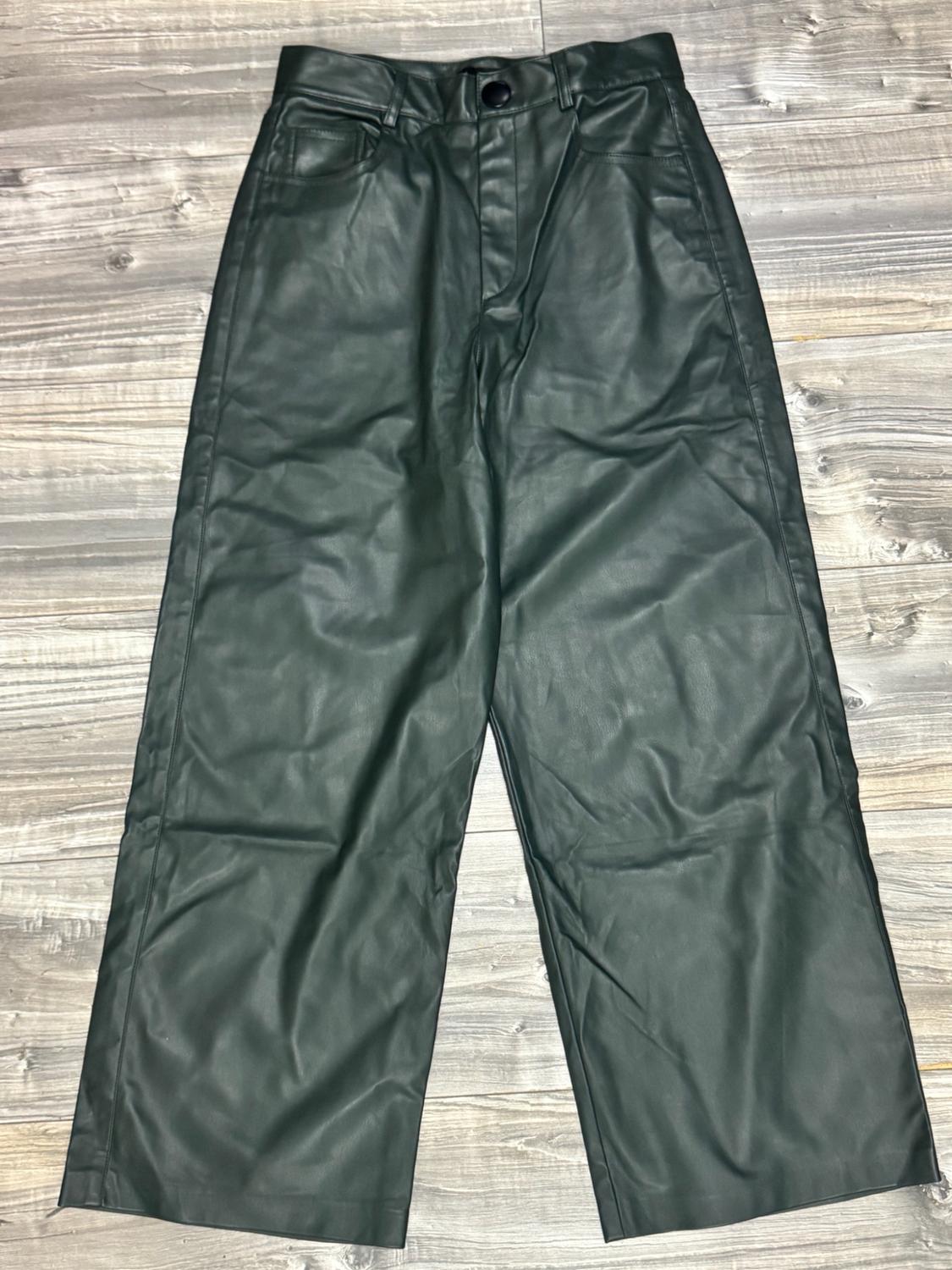 Dark green wide-leg trousers with a glossy finish, button fastening and front pockets, laid out on a wooden floor.