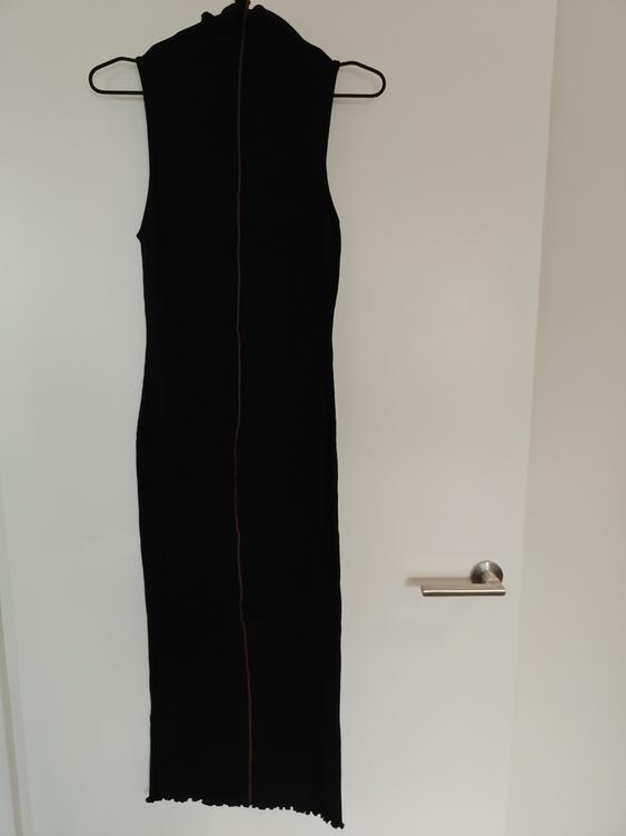 Sleeveless black dress hanging on a hanger over a white door. It has a vertical line on the back.