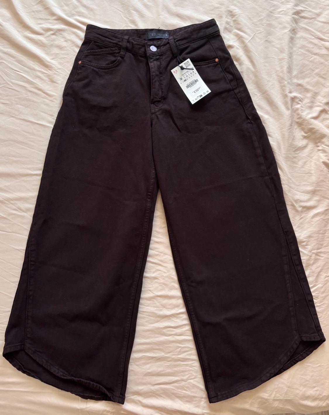 Dark wide-leg trousers with a Zara label, laid out on a light-coloured crumpled fabric.