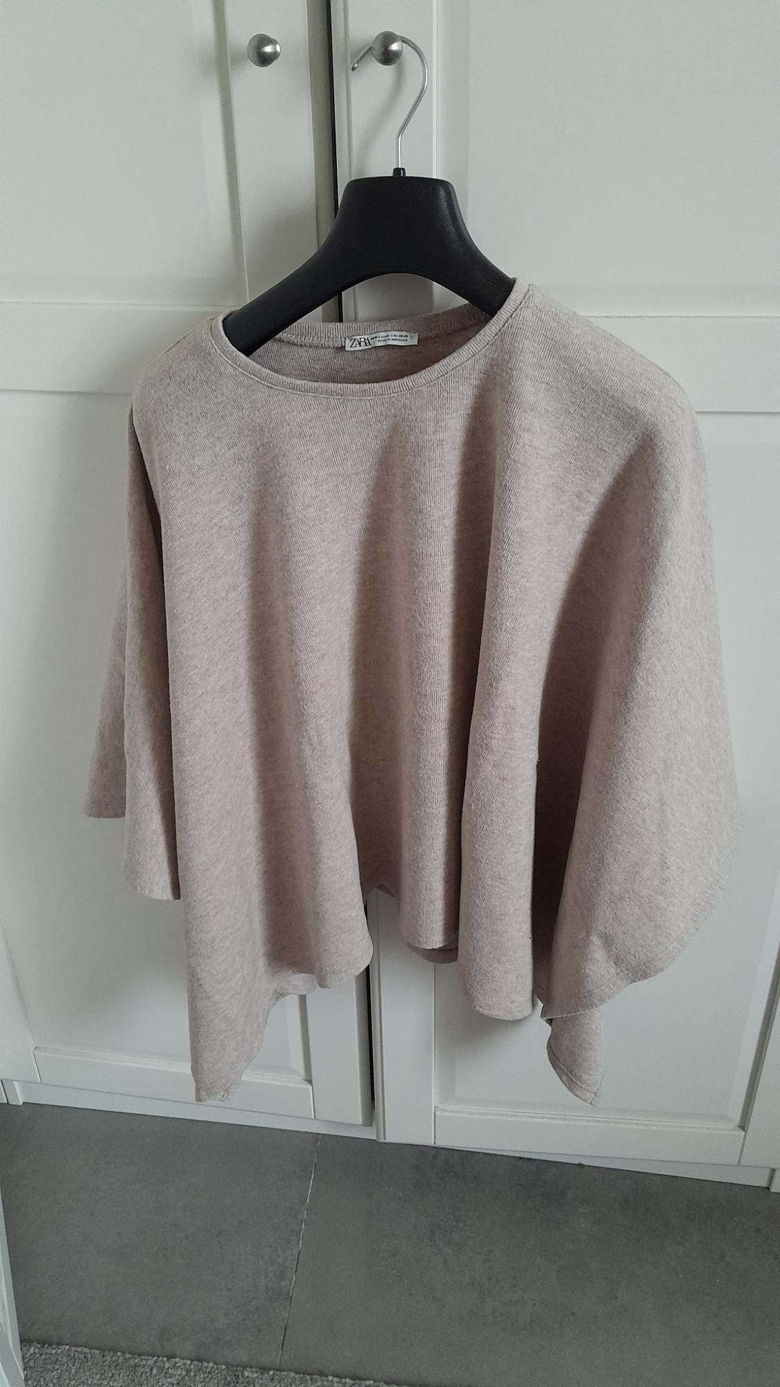 Beige long-sleeved jumper hanging on a black hanger in front of a white wardrobe. Label visible on the collar.