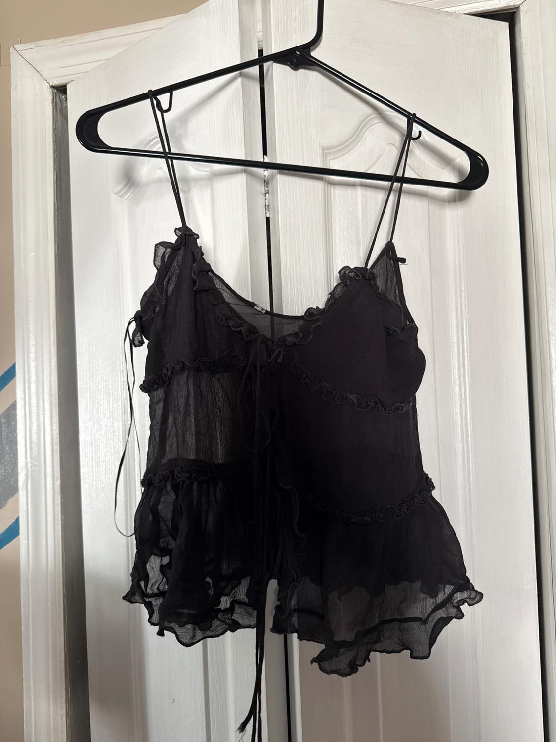 Black spaghetti strap top with ruffles hanging on a black hanger over a white door.