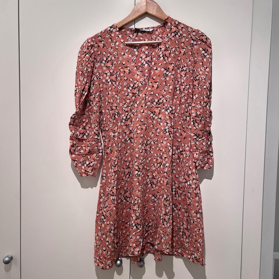Pink dress with a black and white floral print, long sleeves, hanging on a wooden hanger against a white background.