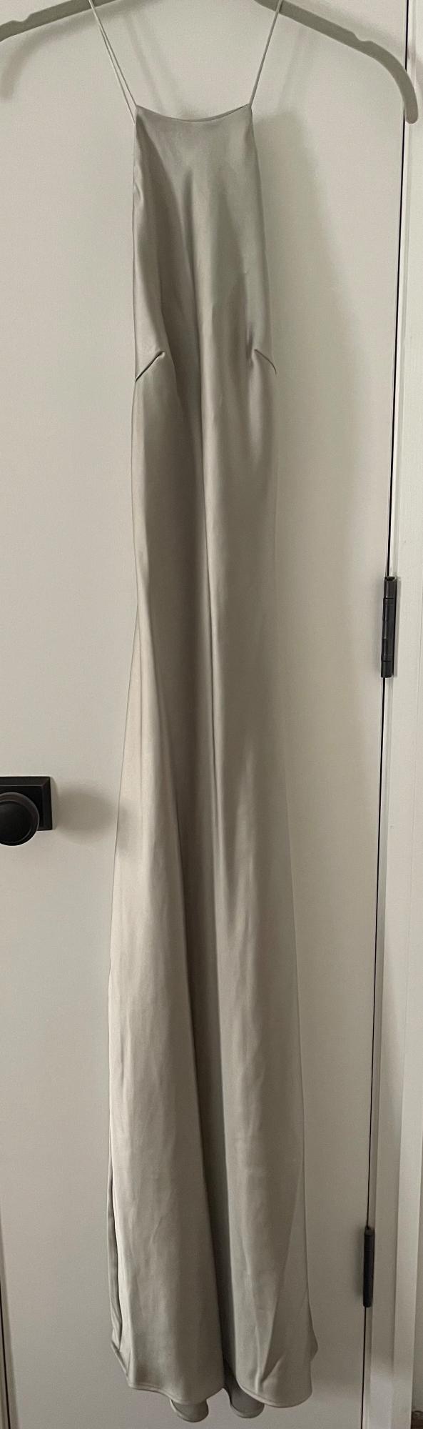 Light grey satin maxi dress with thin straps, hanging on a hanger on a white door with a black doorknob. Minimalist style.