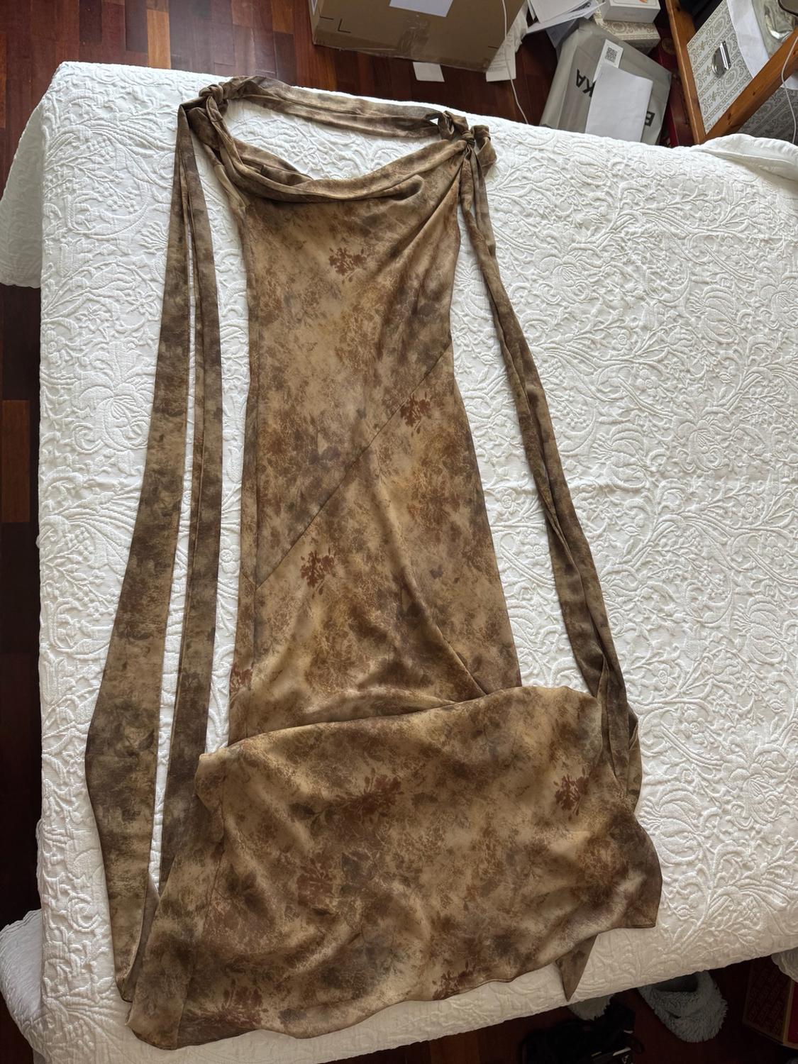 Brown patterned maxi dress with a halter neck and long straps, laid out on a bed with a white bedspread.