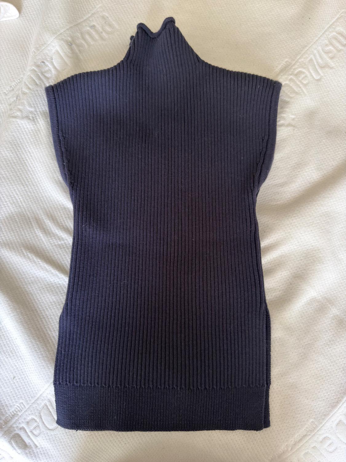 Navy blue ribbed knit top, sleeveless with a high neck, on a textured white surface in a relaxed composition.