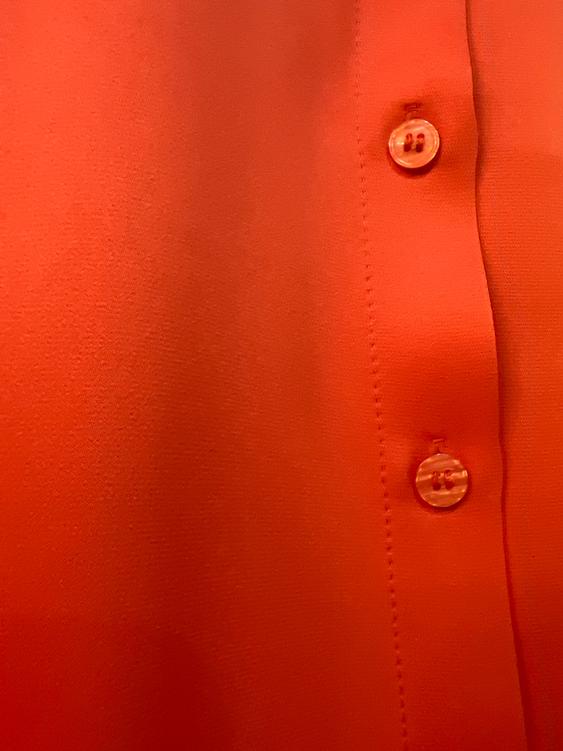Orange shirt with visible buttons in the foreground. Smooth and shiny fabric, highlighting the texture and vibrant color.