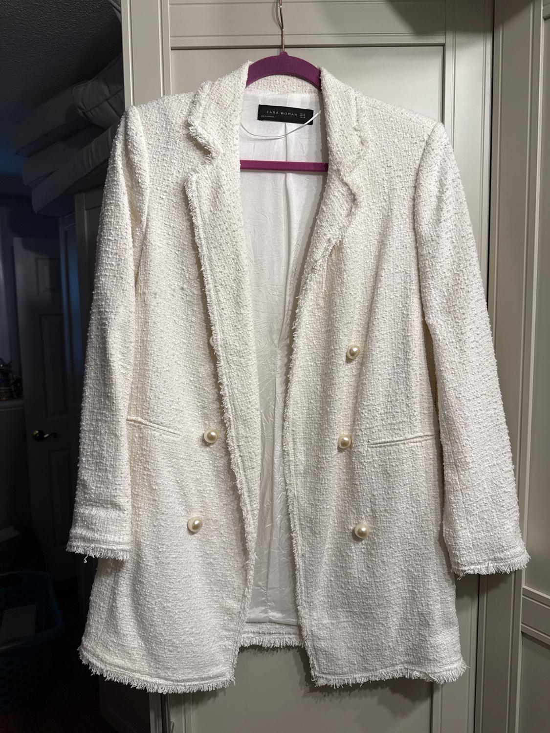 Rough-textured white jacket hanging on a purple hanger. Large buttons and visible label that reads "Zara Woman."