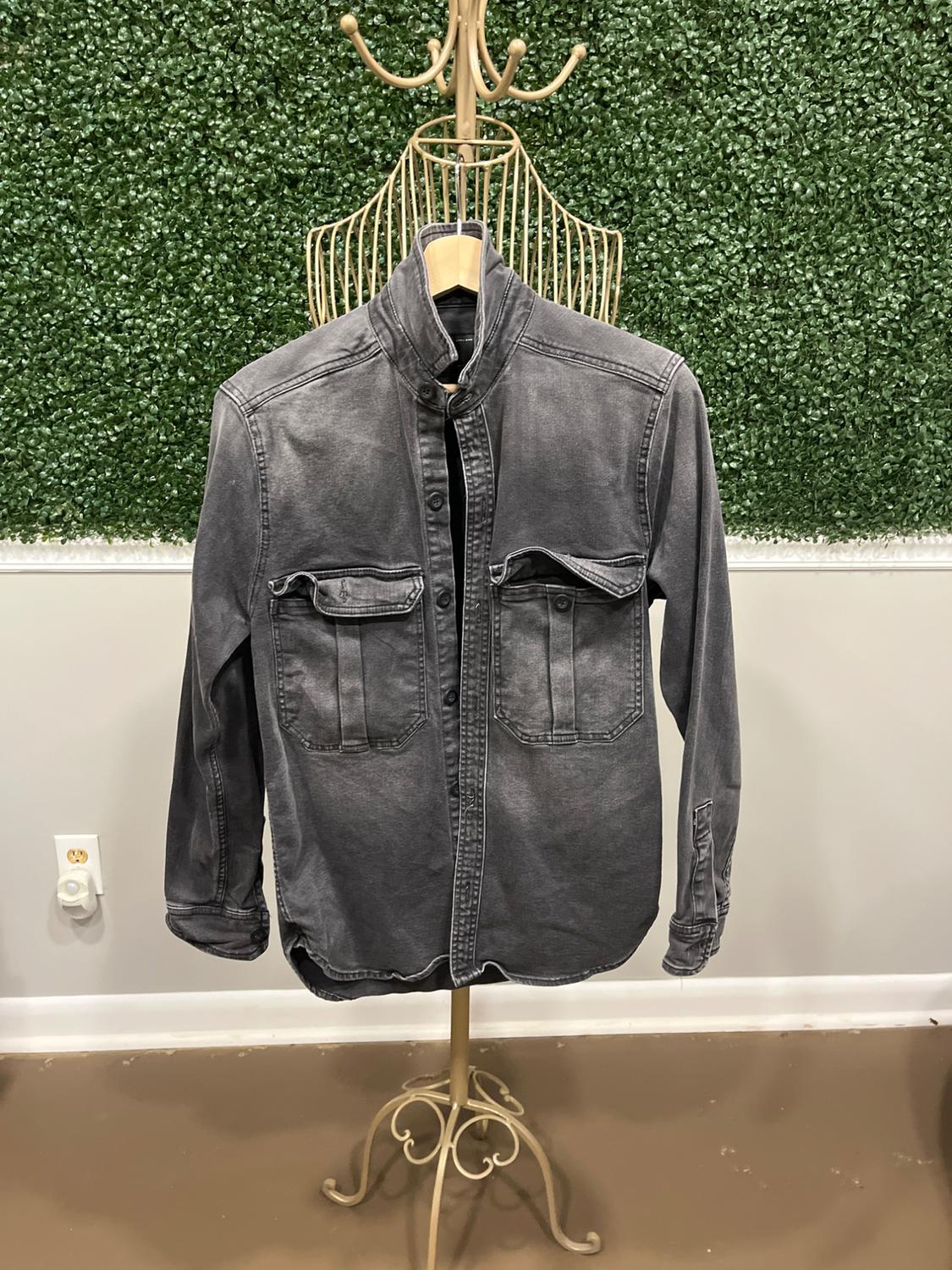 Gray denim jacket hanging on a gold coat rack, green wall background with leaf texture.