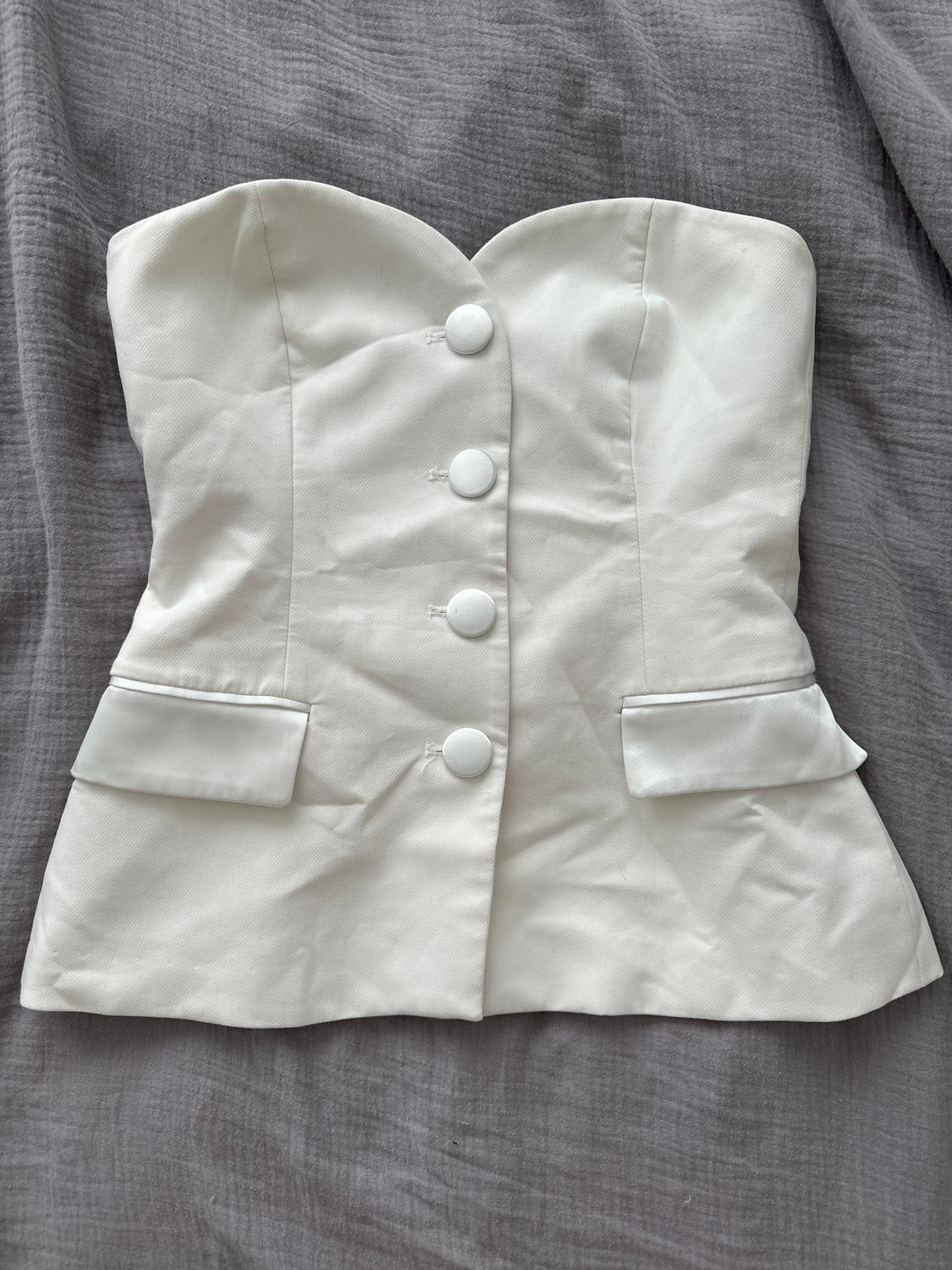 Strapless white corset with large buttons and lapels, on wrinkled grey fabric.