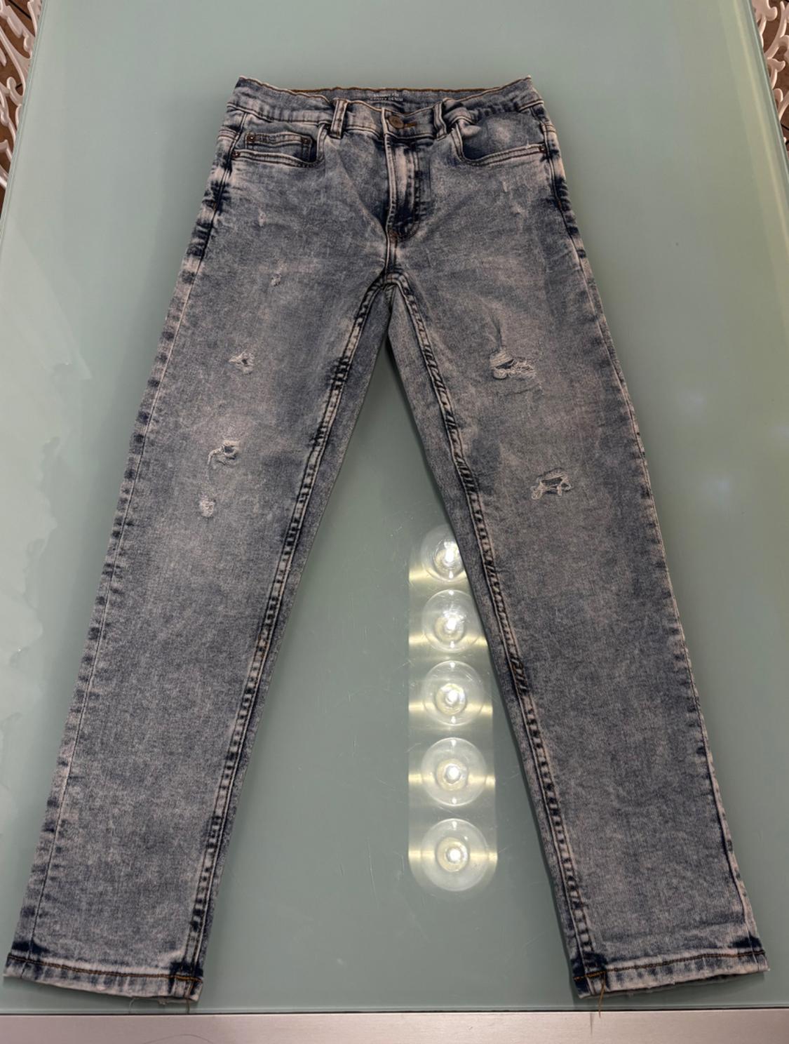 Distressed blue denim jeans with rips, placed on a glass table with circular lights underneath.